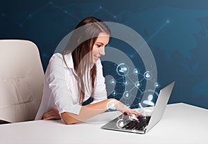 Young lady sitting at desk and typing on laptop with social network icons