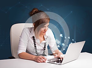 Young lady sitting at dest and typing on laptop with message icons comming out