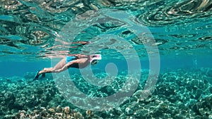 Young lady snorkeling over coral reefs in a tropical sea. Woman with mask snorkeling in clear water