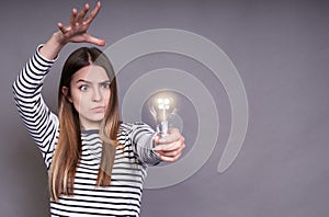 A young lady in a striped jacket holds a light bulb in her hand