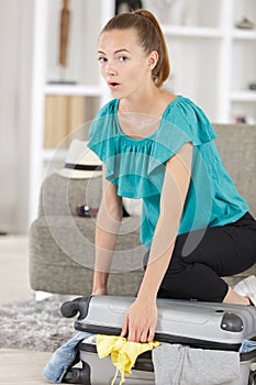 Young lady struggling to close bulging suitcase