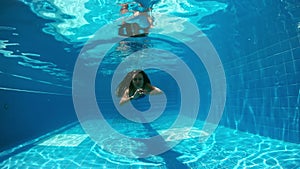 Young lady swimming underwater in the pool. Underwater woman portrait in swimming pool.