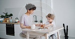 Young lady teaching small boy to roll dough cooking pastry at home in kitchen