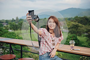 Young lady traveler taking selfie with her camera in outdoors cafe with beautiful nature landscape