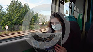 A young lady travels by train in a medical mask and reads a newspaper
