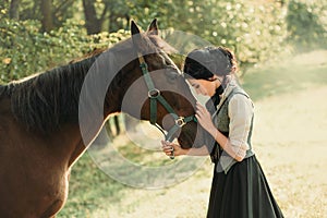 A young lady in a vintage dress, with tenderness and with affection hugs her horse. An ancient, collected hairstyle, a