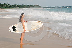 Young lady walking with surf board on sandy tropical beach