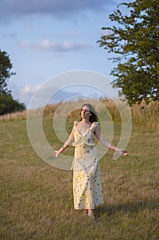 A young lady walks barefoot in a field at sunset