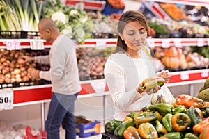 Young latin american girl choosing sweet pepper in supermarket