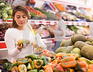 Young latin american girl choosing sweet pepper in supermarket with her boyfriend