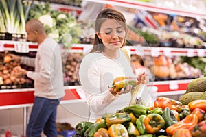 Young latin american girl choosing sweet pepper in supermarket other vegetables