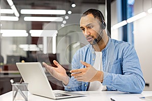 A young Latin American man in a headset works in the office on a laptop, conducts an online consultation and business