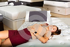 Young latin american woman lying on bed in furniture store