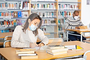 Young latin american woman in protective mask studying in library