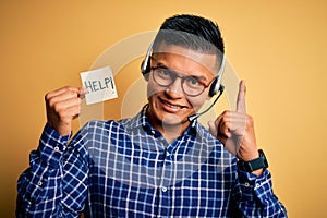Young latin call center agent man overworked holding help message paper using headset surprised with an idea or question pointing
