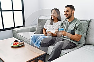 Young latin couple having breakfast sitting on the sofa at home
