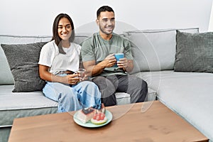 Young latin couple having breakfast sitting on the sofa at home