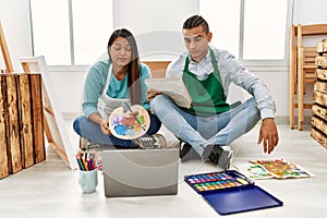 Young latin couple having online paint class at art studio thinking attitude and sober expression looking self confident