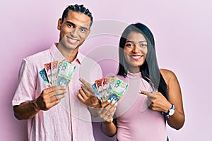 Young latin couple holding australian dollars smiling happy pointing with hand and finger