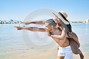 Young latin couple hugging and pointing to the horizon with finger at the beach