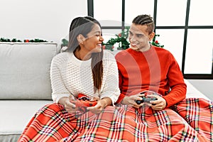 Young latin couple playing video game sitting on the sofa at home