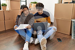 Young latin couple with serious expression using laptop sitting on the floor at new home