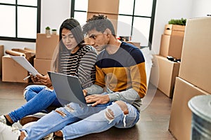 Young latin couple with serious expression using laptop sitting on the floor at new home