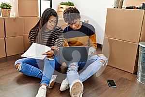 Young latin couple with serious expression using laptop sitting on the floor at new home