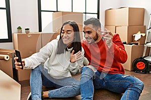 Young latin couple smiling happy doing video call using smartphone at new home