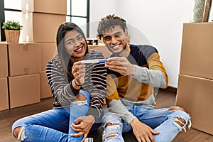 Young latin couple smiling happy holding pregnancy test sitting on the floor at new home