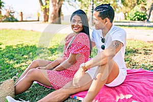 Young latin couple smiling happy and hugging sitting on the grass at the park