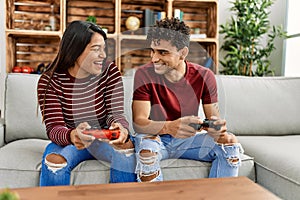 Young latin couple smiling happy playing video game sitting on the sofa at home