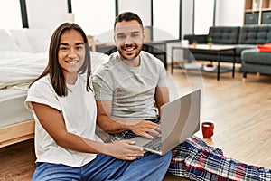 Young latin couple smiling happy using laptop sitting on the floor at bedroom