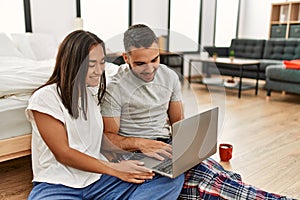 Young latin couple smiling happy using laptop sitting on the floor at bedroom