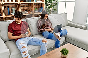 Young latin couple smiling happy using laptop and smartphone at home