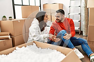 Young latin couple smiling happy using smartphone at new home