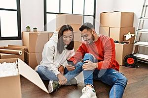 Young latin couple smiling happy using smartphone at new home