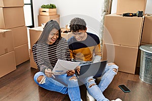 Young latin couple using laptop sitting on the floor at new home