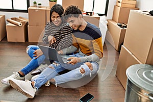 Young latin couple using laptop sitting on the floor at new home