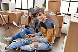 Young latin couple using laptop sitting on the floor at new home