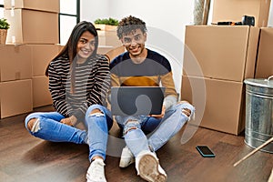 Young latin couple using laptop sitting on the floor at new home