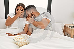 Young latin couple watching scary movie lying on bed