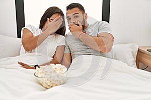 Young latin couple watching scary movie lying on bed