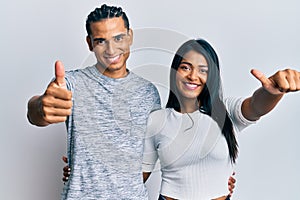 Young latin couple wearing casual clothes approving doing positive gesture with hand, thumbs up smiling and happy for success