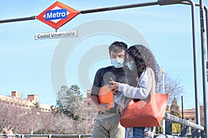 Young latin couple wearing protective face mask looking at the smartphone at Ciudad Universitaria train stop photo