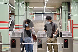 Young latin couple wearing protective face mask walking through subway turnstile at the train or metro station