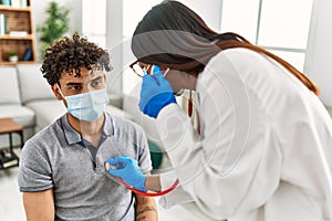 Young latin doctor woman auscultate heart man using stethoscope at medical room photo