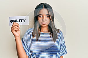 Young latin girl holding quality word on paper thinking attitude and sober expression looking self confident