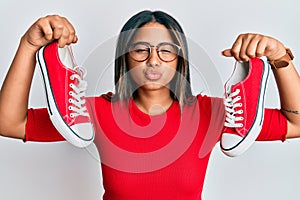 Young latin girl holding red casual shoes looking at the camera blowing a kiss being lovely and sexy