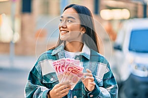 Young latin girl smiling happy counting chinese yuan banknotes at the city